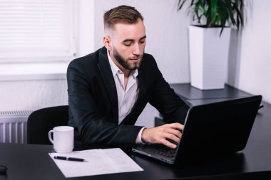 Ofis masasında dizüstü bilgisayarın önünde oturan yakışıklı yönetici.