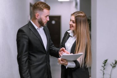 Patron ve genç astları ofis koridorunda evrakları kullanarak konuşuyorlar.