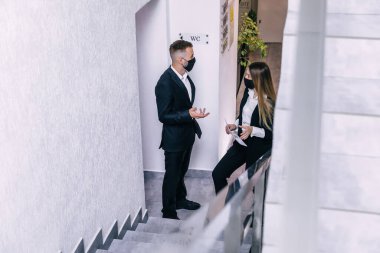 Coronavirus sırasında koruyucu maskeler takan iki meslektaşı ofiste ayakta duruyor ve mali sonuçları ve krizi tartışıyorlar.