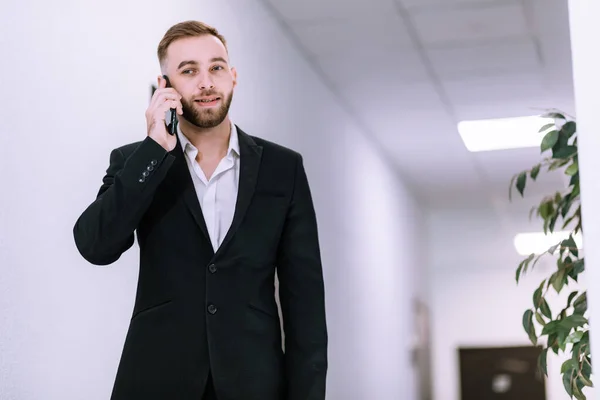 Successful business man have telephone conversation while standing in empty office corridor. Male professional banker in suit talking on mobile phone during work break.