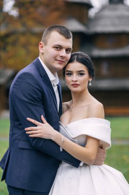 Sonbaharda eski kilisenin arka planında beyaz bir elbise içinde sevgili gelin ve damat. Romantik yeni evlilerin düğün portresi.