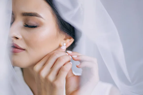 一个穿着白袍 头戴面纱 发型的漂亮新娘会把耳环戴在耳朵上 婚纱照 — 图库照片