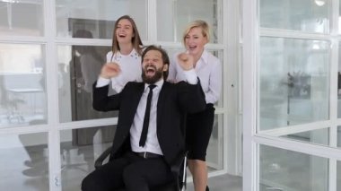 Neşeli iş ekibi başarıyı kutluyor. Üç çılgın iş arkadaşı ofis koridorunda sandalyeye binip gülüyor, bağırıyor ve eğleniyorlar.