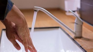Adamın elleri, ellerini deri yıkama köpüğüyle lavaboda yıkıyor ve su ellerinden aşağı akıyor. Sağlık, temizlik ve ellerle koronavirüs teması kavramı