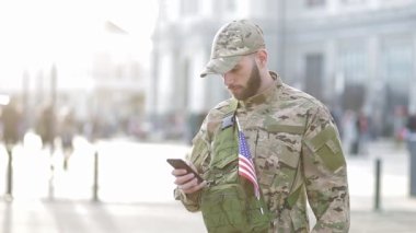Sokakta duran şapkalı yakışıklı bir erkek askerin portresi. Askerler telefona bakar..