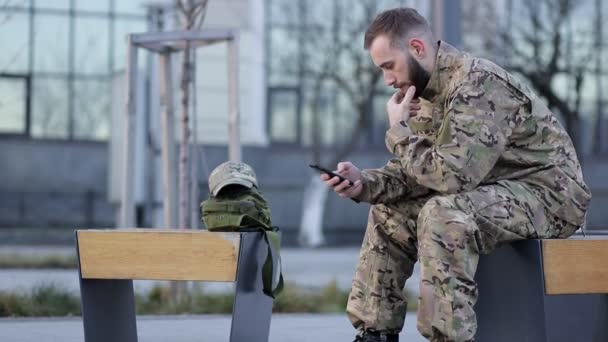 Ένας Λυπημένος Στρατιώτης Στολή Κάθεται Ένα Παγκάκι Στο Δρόμο Κοντά — Αρχείο Βίντεο