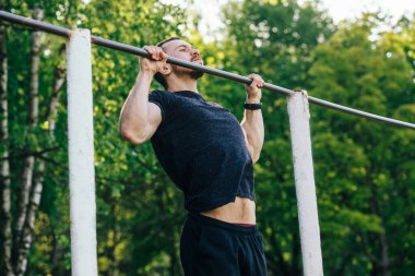 Bir adam sahaya spor yapmaya gider, yaz günü barın önünde kendini yukarı çeker.