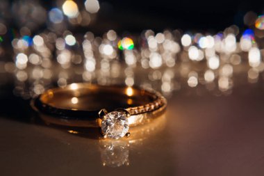 Ahşap bir masanın üzerindeki zarif elmas yüzük ampullerin arka planına karşı. Aşk ve düğün kavramı