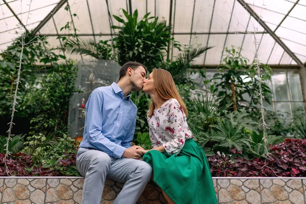 年轻夫妇坐在长椅上 在一个绿色的植物园里接吻 — 图库照片