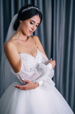 Makyajlı ve duvak takan mutlu kız gelini düğün günü toplanırken nazikçe gülümsüyor.