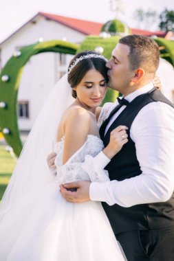 Yeşil bir yaz bahçesinde yeni evliler kucaklaşır. Mutlu gelin ve damat. Romantik evli genç bir aile.