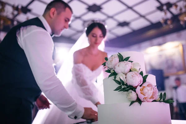 花嫁と新郎は宴会で花で飾られた白いウェディングケーキを切りました — ストック写真