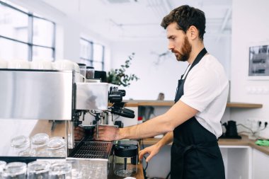 Profesyonel, deneyimli bir barista kahve makinesinde kahve hazırlar, siyah önlük ve beyaz tişört giyer..