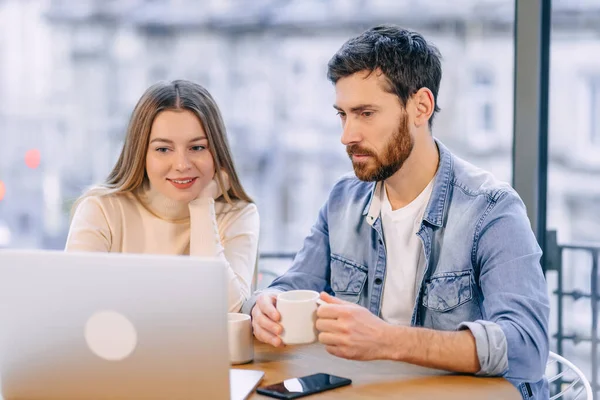 Beautiful couple working on a laptop in a cafe. Happy young man and gorgeous woman smiling, using laptop, sitting at a table in a restaurant.