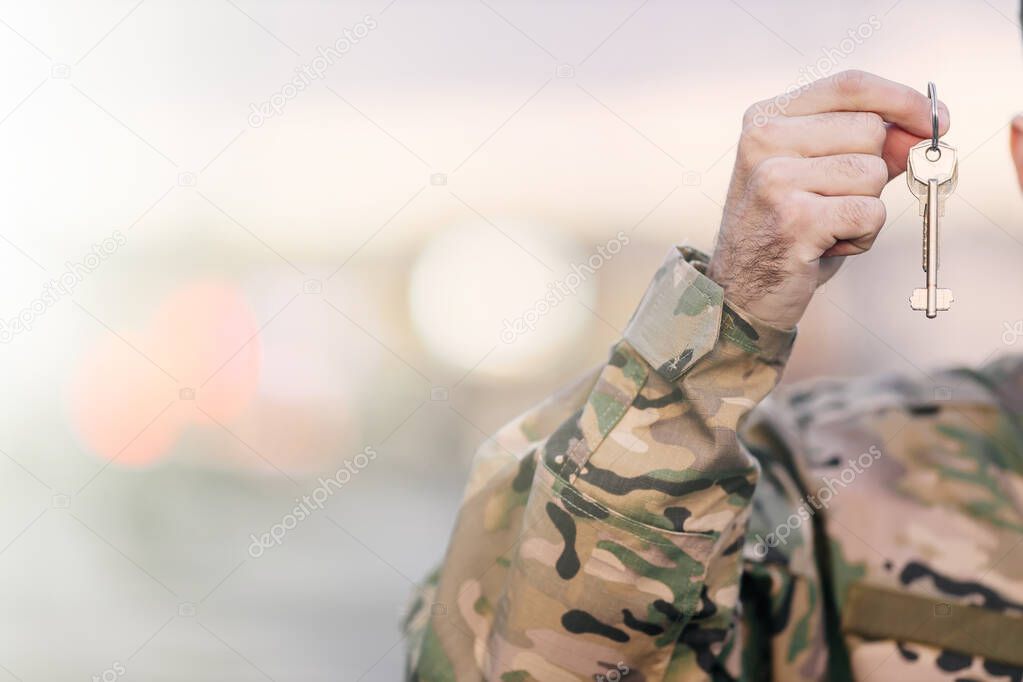 the hand of a patriotic military man in uniform holding the keys on a crumpled background. Buying a property
