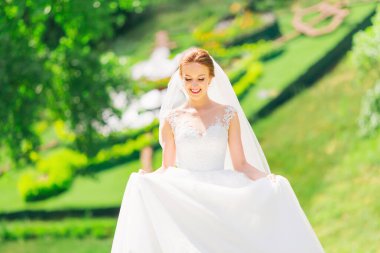 Uzun elbiseli, güzel, gülümseyen bir esmer gelin yeşil çayırlarda yürüyor.