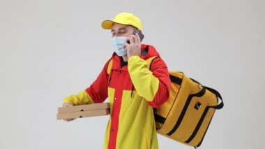 Tıbbi maskeli bir kurye pizza için karton kutular tutuyor, müşteriyi cep telefonuyla arıyor..