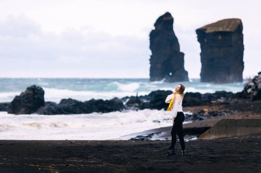 Gülümseyen kız İzlanda 'daki volkanik kumsalda yürüyor bulutlu gökyüzünün ve dağların arkasında.