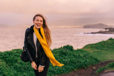 Bir kadın zirvenin kenarında duruyor, arka planda İzlanda doğası: kara topraklar, Atlantik Okyanusu ve volkanik kayalar ve yeşil doğa..