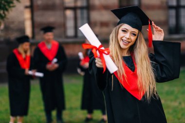 Akademik elbisesi ve mezuniyet şapkası takmış, elinde diplomasıyla gülümseyen beyaz saçlı kız öğrenci arkadaşlarının ve üniversitenin geçmişine karşıydı..