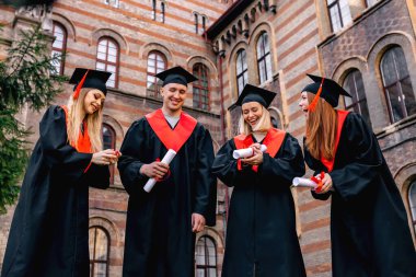 Bekar kıyafetleri içinde mutlu öğrenciler ve törenden sonra dışarıda yürüyen diplomalarla..