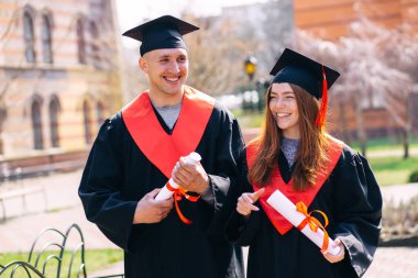 Gülümseyen sınıf arkadaşları ve erkek üniversite mezunları diplomalarıyla birlikte palto giymiş. Üniversite konseptinden mezun olmak