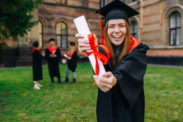 Cheerful graduate girl in an academic gown. Shows a scroll with a red ribbon. Enjoy graduating from university.