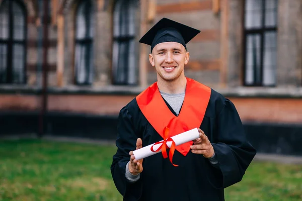 happy student in academic dress and hat holding university or academy certificate. Graduate concept.