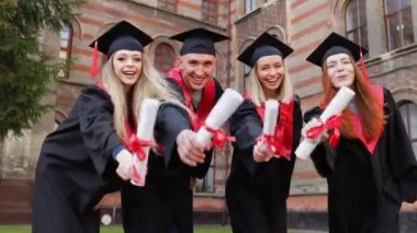Mezuniyet gününde akademik giysiler ve şapkalar içinde selfie çeken, diploma sallayan, fotoğraf çeken mutlu bir grup yetişkin öğrenci..