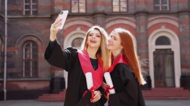 Güzel bir kadın diplomalı selfie çekiyor, kırmızı kurdele parşömeni akıllı telefon kullanıyor, genç kadınlar poz veriyor.