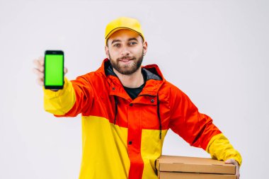 Sırt çantasında sarı termal çantalı gülümseyen teslimatçı akıllı telefon gösteriyor, beyaz arka planda izole edilmiş. Boş yeşil ekranlı telefonu kullanan adam.
