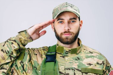 Kamuflaj üniformalı bir Amerikan askerinin portresi, selam veriyor, kameraya bakıyor. Asker saygı göstergesi olarak elini başına dayadı..