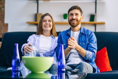 Neşeli çift gülümsüyor ve evde kanepede oturup televizyon izliyor ve patlamış mısır yiyor.