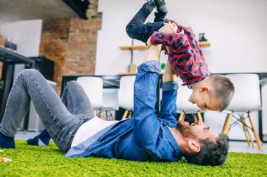Şefkatli bir baba oğlunu kucağına alır, uzanmış ellerle uçuyormuş gibi yapar, mutfakta sıcak zeminde yatar, aile eğlenceli şeyler yapar.