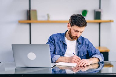 Ciddi bir iş adamı dizüstü bilgisayarda çalışıyor ve bir deftere bir şeyler yazıyor. Kariyer dünyası konsepti.