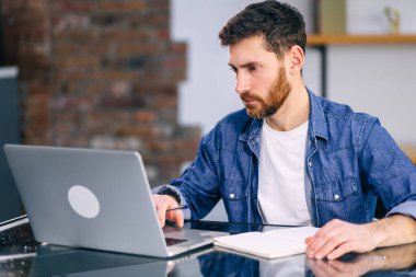 Düşünceli işadamı iş yerinde dizüstü bilgisayara bakan online bir proje düşünüyor, rüya gibi profesyonel çözümler düşünüyor çalışma masasında bilgisayarla oturuyor, öğrenci aranıyor ofis kafesinde yeni fikirler yaratılıyor.