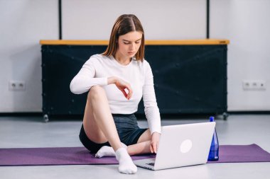 Çekici genç bir kadın yogaya hazırlanıyor, bilgisayardaki işgalin videosunu arıyor. Kişisel izolasyon yararlı, eğlenceli ve çevrimiçi eğitimdir. Sağlıklı yaşam tarzı kavramı.