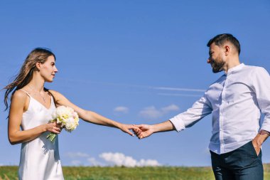 Genç aşıklar, erkek ve kadın, mavi gökyüzü ve yeşil çimlerin arka planında el ele tutuşuyorlar..