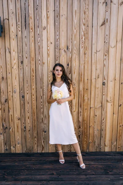木製の壁に対して花束を保持裸の肩を持つ白いドレスで美しい花嫁 — ストック写真