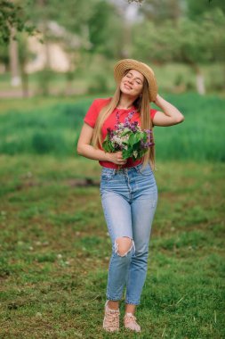 Bahar bahçesinde, her gün giydiği kıyafetlerle bir buket leylakla genç ve çekici bir kadının fotoğrafı. Bahar arkaplanı.