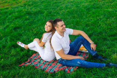 young couple resting on a plaid blanket on a green field. The newlyweds spend free time together.