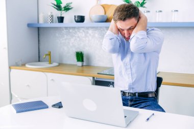 Boyun ağrısı. Dizüstü bilgisayarda çalışan yorgun genç bir adam odadaki masada oturuyor..