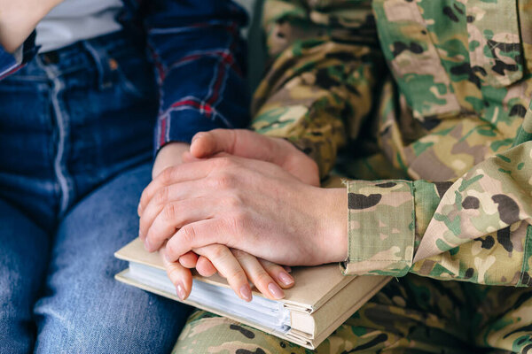 close-up of the hands of the beloved bet, a woman and a man in camouflage. They keep their hands on their wedding album, memories. The girl escorts the soldier to the army.