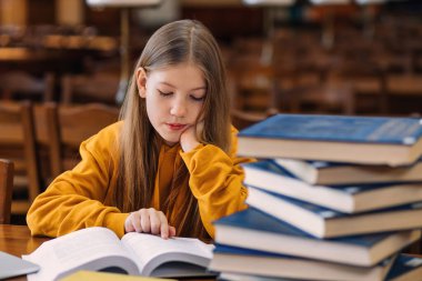 Sevimli küçük bir kız kitapçıda ya da okul kütüphanesinde oturuyor, kitap okuyor, ödevlerini yapıyor.