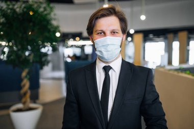 İş adamı ve koronavirüs. Ofisin koridorunda duruyor, yüzünde virüslere, bakterilere, mikroplara, enfeksiyonlara ve gribe karşı koruyucu bir maske takıyor..