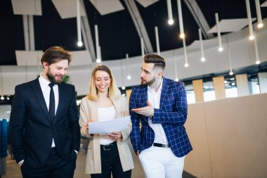 three young business people, prowling the corridors of an office building, discussing a document or a project.