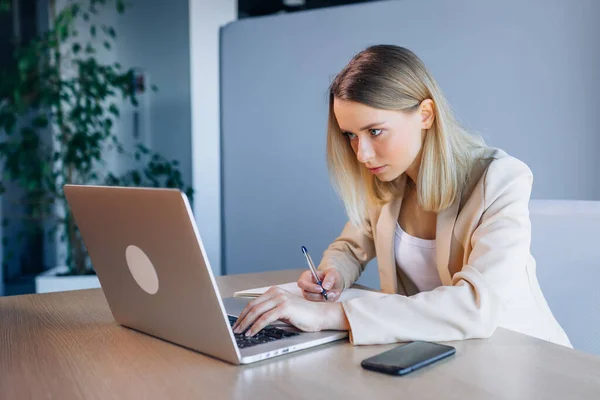 Dziewczyna Patrzy Ekran Laptopa Biurze Poważna Młoda Kobieta Robi Notatki — Zdjęcie stockowe