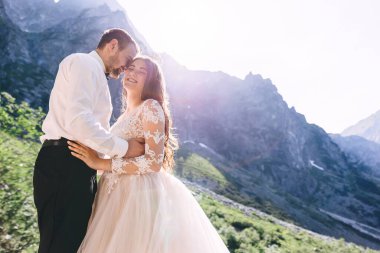 Dağda yaşayan modaya uygun yeni evliler. Şık gelinlikli, kıvırcık saçlı, gün batımında sarılan gelin.