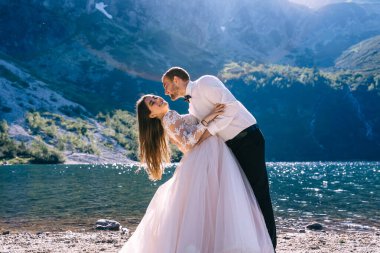 Yeni evlilerin göl kenarında, arka planda dağların karşısında kucaklaşmalarını ön planda görmek. Düğün konsepti