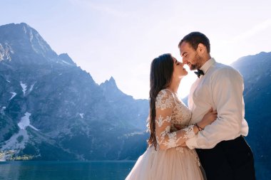 Yeni evliler birbirlerine bakar, göle ve günbatımına bakarak..